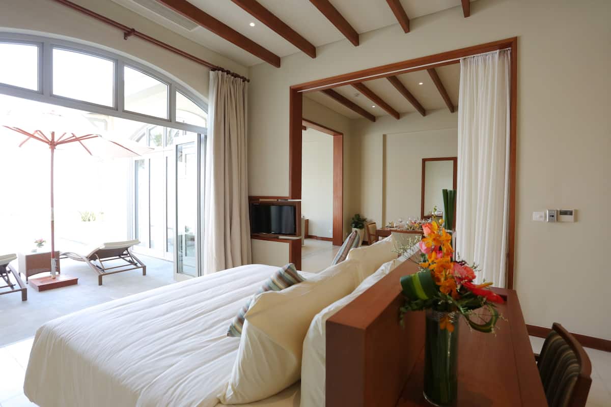 A hotel room with a large bed, a wooden desk, a television, and a large window with curtains.