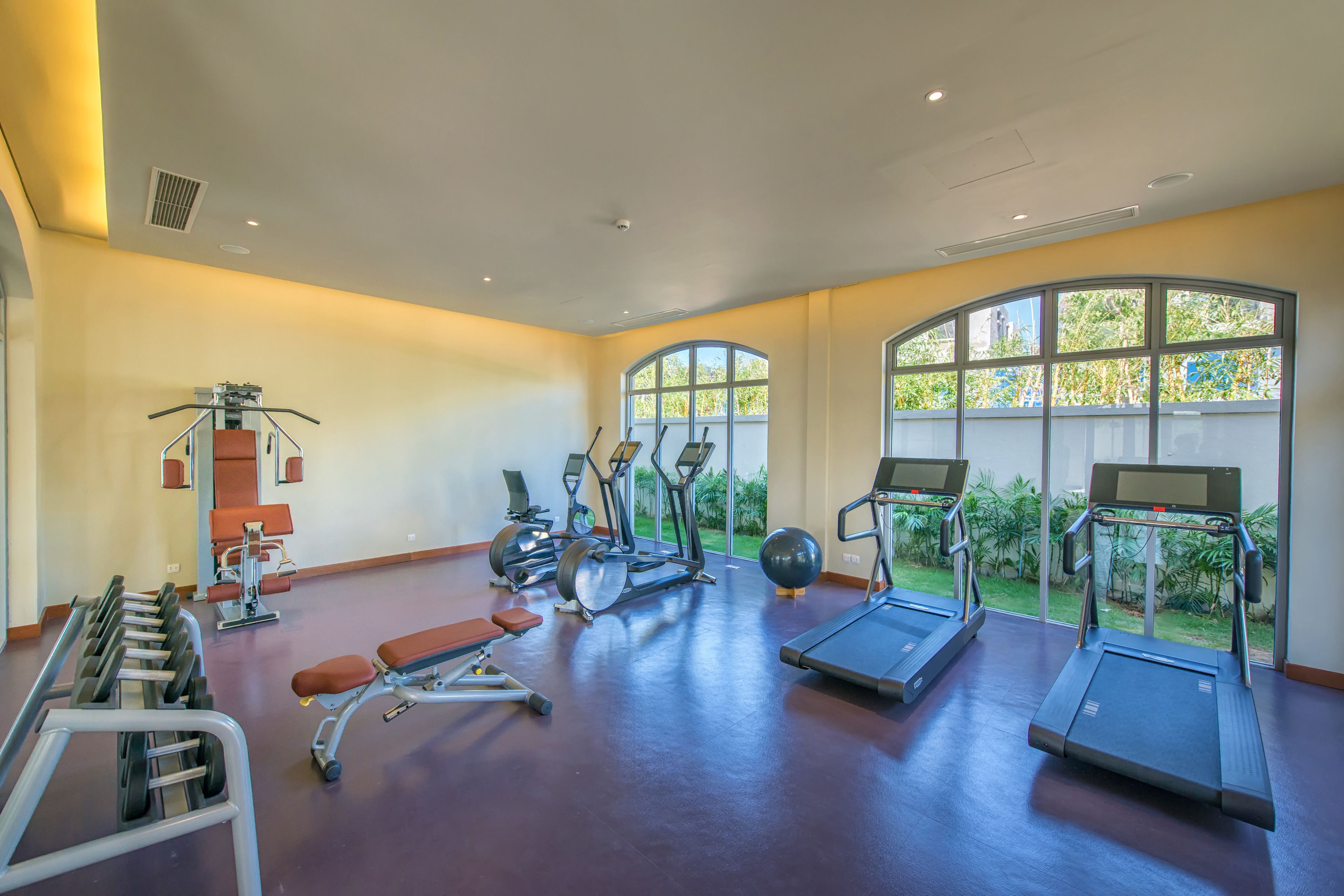 A spacious gym with various exercise equipment, large windows, and a clean, modern design.