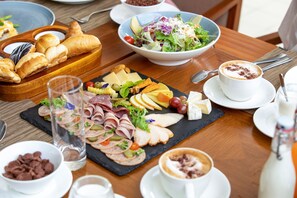 A breakfast buffet with various cheeses, meats, and pastries on a wooden table. - FLC Luxury Resort Samson (Sam Son)