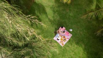 A person sitting on a blanket with a picnic setup in a grassy area surrounded by trees.