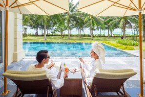 A couple sitting at a table with a view of a pool and palm trees. - FLC Luxury Resort Samson (Sam Son)