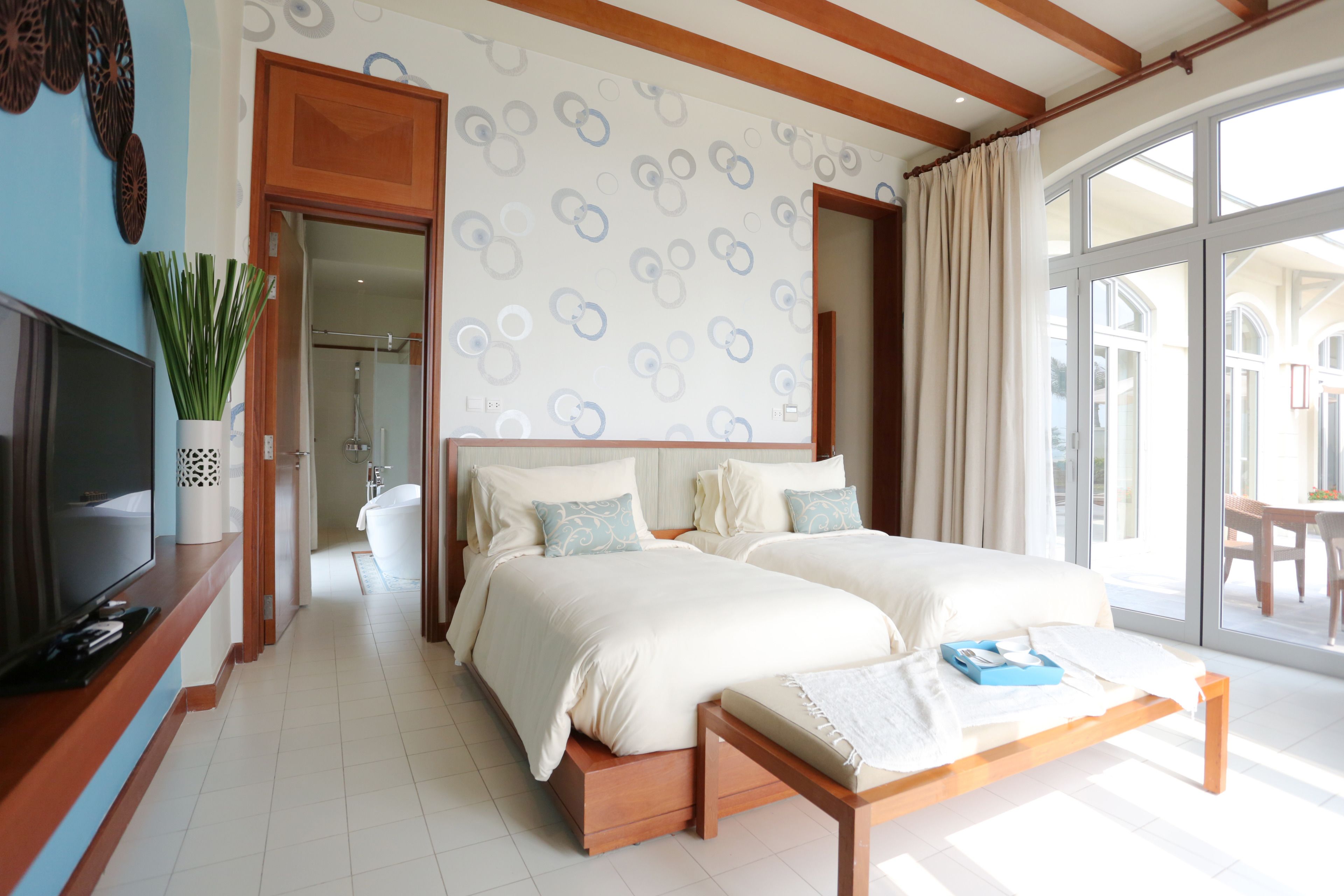 Habitación de hotel con dos camas, televisión, planta y ventana grande.