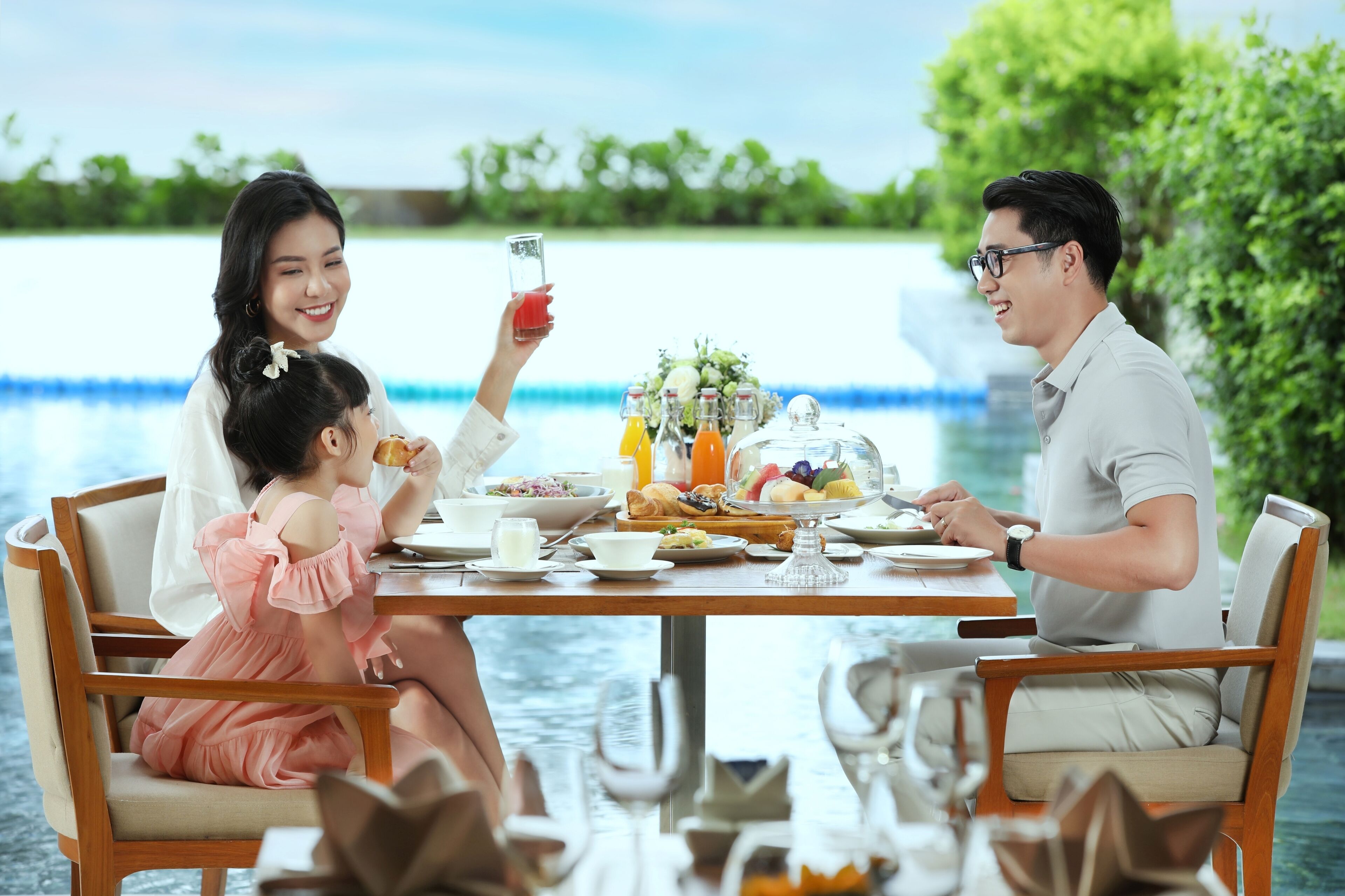 A dining table with food and drinks, a glass of juice, and a vase of flowers.