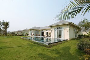 A modern house with a swimming pool, a well-maintained lawn, and a patio area with outdoor furniture. - FLC Luxury Resort Samson (Sam Son)