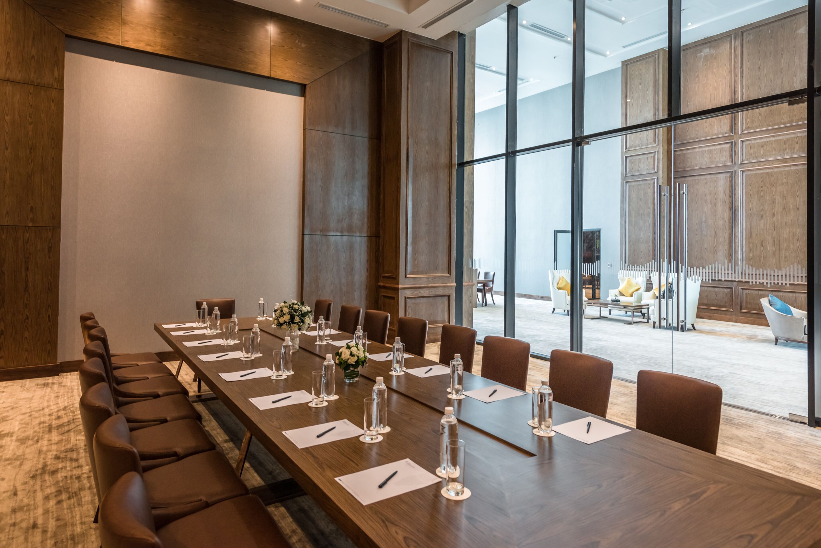 A conference room with a long table, chairs, and glassware, with a large window and a view of the outdoors.
