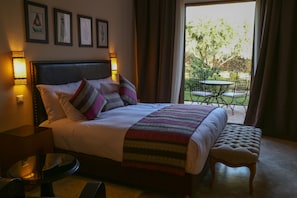 Quarto de hotel com uma cama grande, uma mesa redonda pequena e vista para o exterior através de uma porta deslizante.