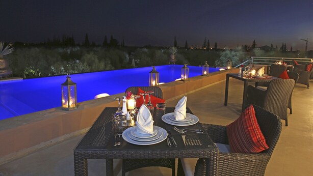 Un área de comedor al aire libre con mesas preparadas para dos, con vista a una piscina.