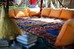 Uma cama com um edredom colorido e almofadas laranja, uma cesta de vime e uma pilha de livros.
