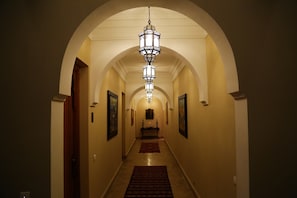 Um corredor com um candelabro, obras de arte emolduradas nas paredes e piso coberto de carpete.