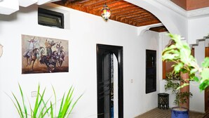 A hallway with a black door, a painting of horsemen, and a potted plant.