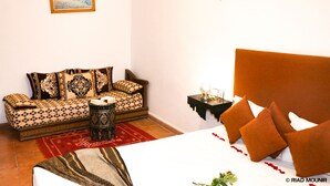A room with a bed, a sofa, a small table, and a wall-mounted lamp.