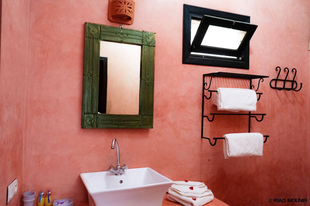 A bathroom with a green-framed mirror, a white sink, and a towel rack with multiple towels.