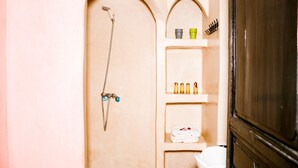 A bathroom with a shower, shelves with toiletries, and a toilet.