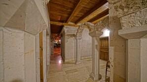 A corridor with stone walls, wooden beams, and a tiled floor.