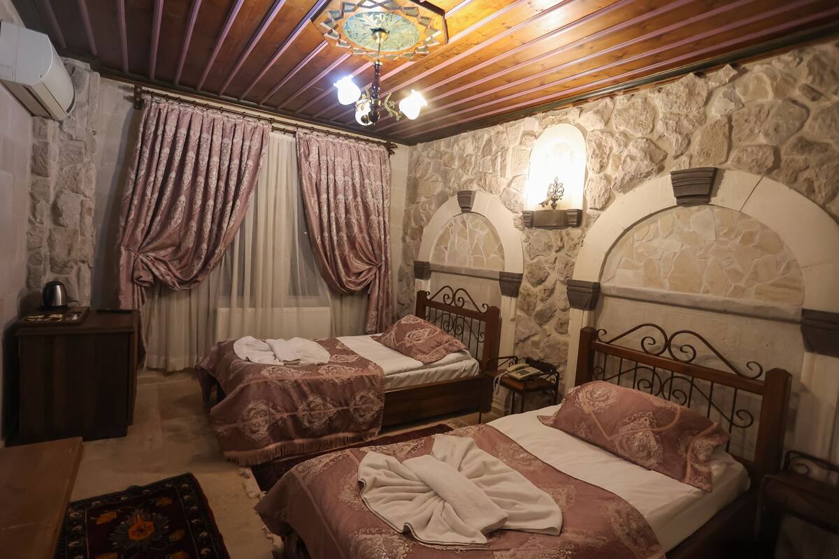 Una habitación con dos camas, paredes de piedra, techo de madera y un candelabro.
