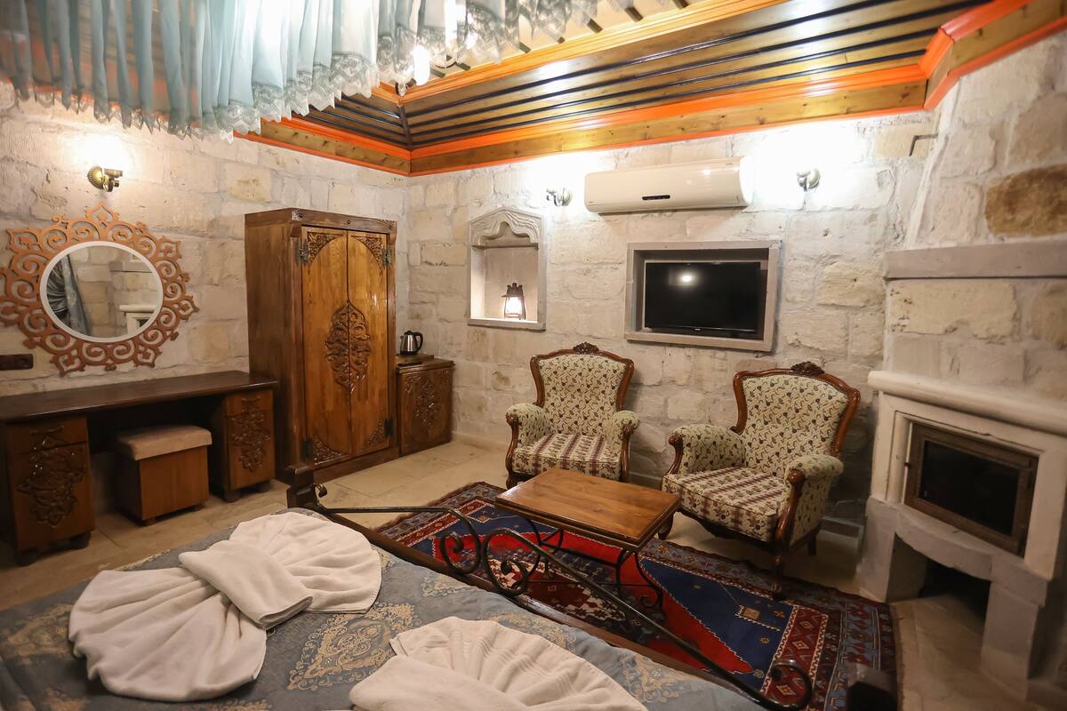 Una habitación con chimenea, dos sillones estampados, una mesa de centro de madera, un espejo y una pared de piedra.