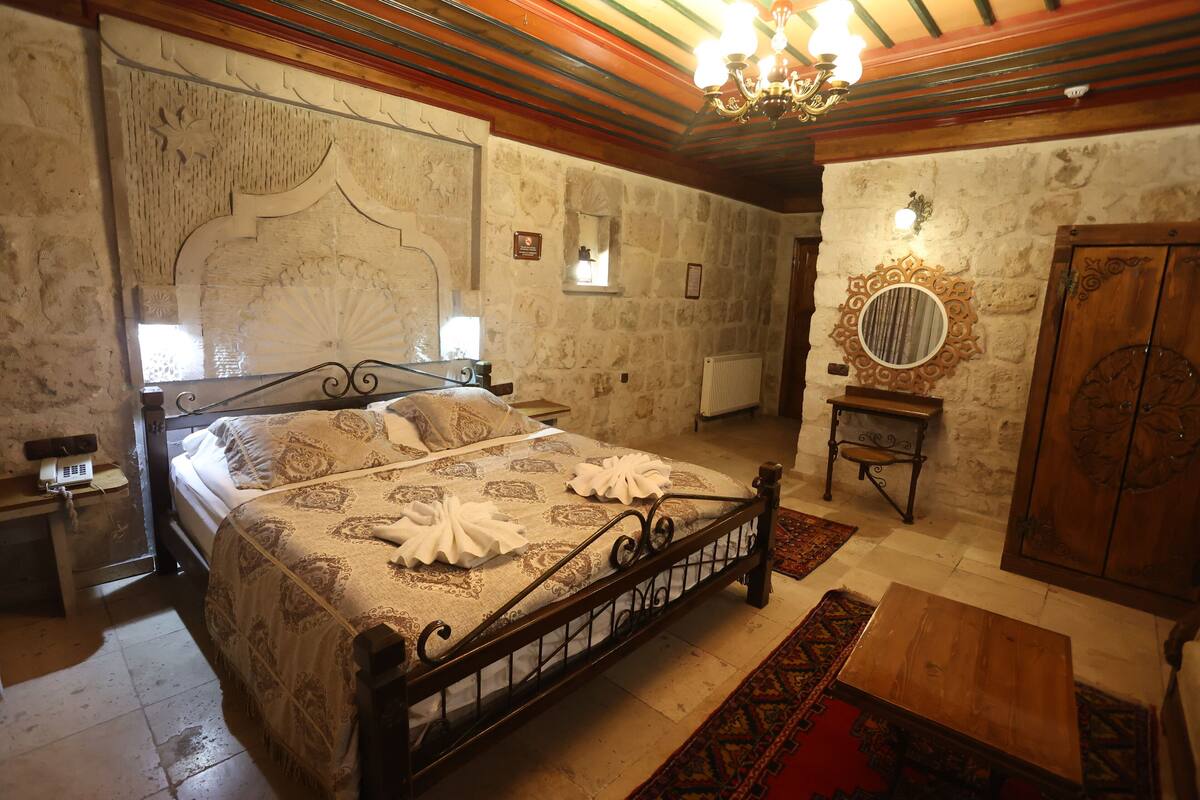 Un dormitorio con una cama grande, un armario de madera, una mesita y una araña.