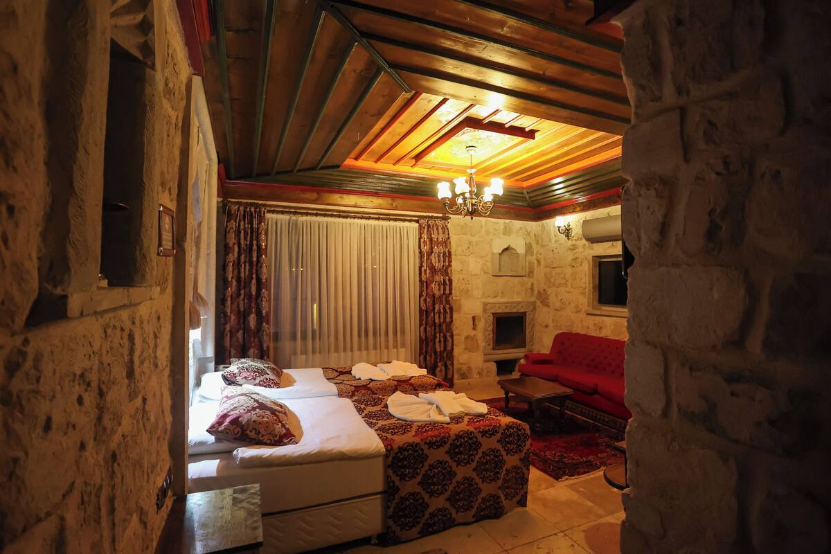 Una habitación con pared de piedra, chimenea, sofá rojo y cama con toallas.