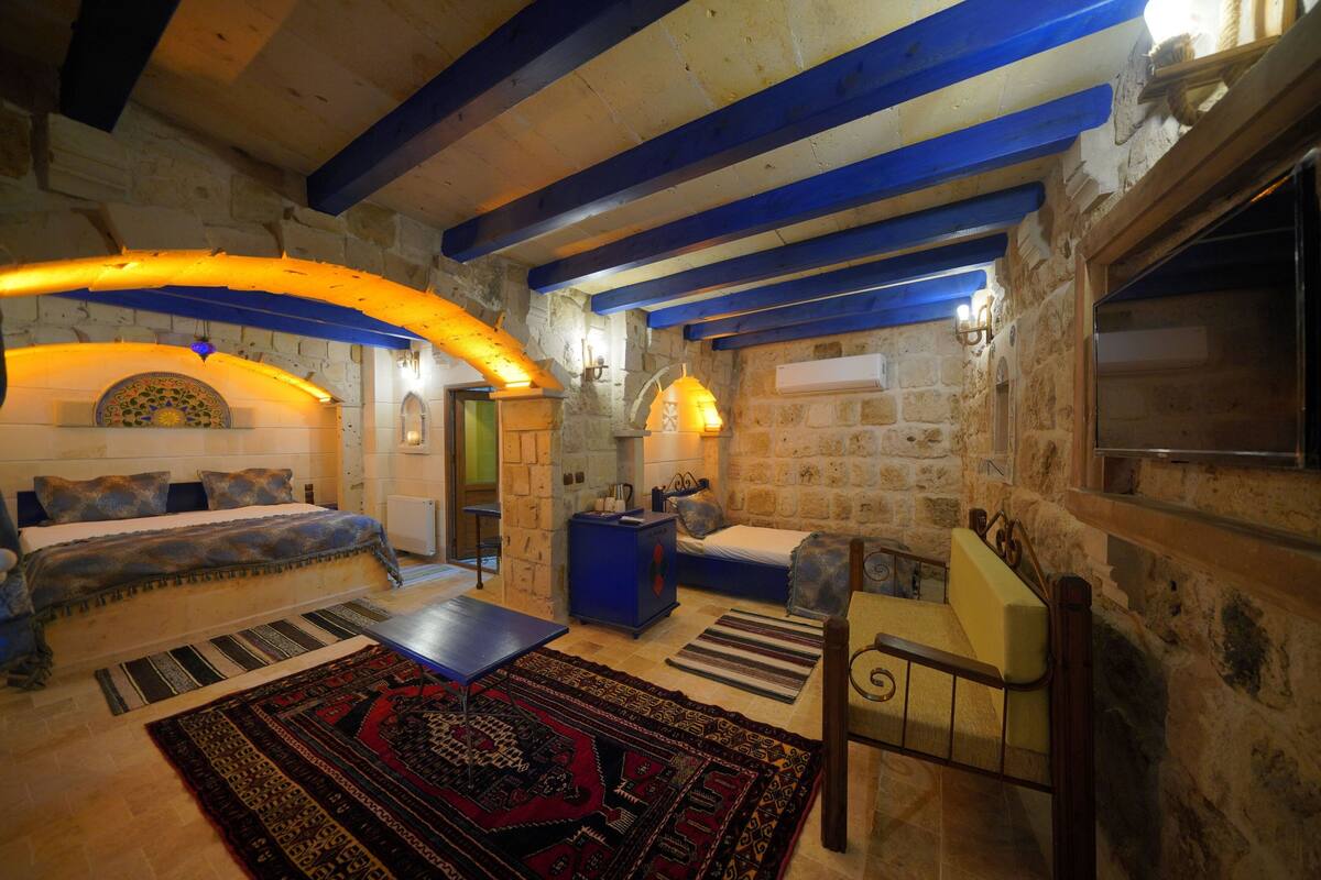 Una habitación acogedora con una pared de piedra, una cama, un sofá azul, una mesita y una silla.