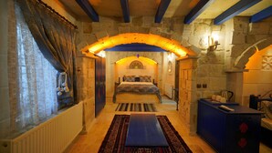 A bedroom with a stone wall, a bed, a blue cabinet, and a window with curtains.