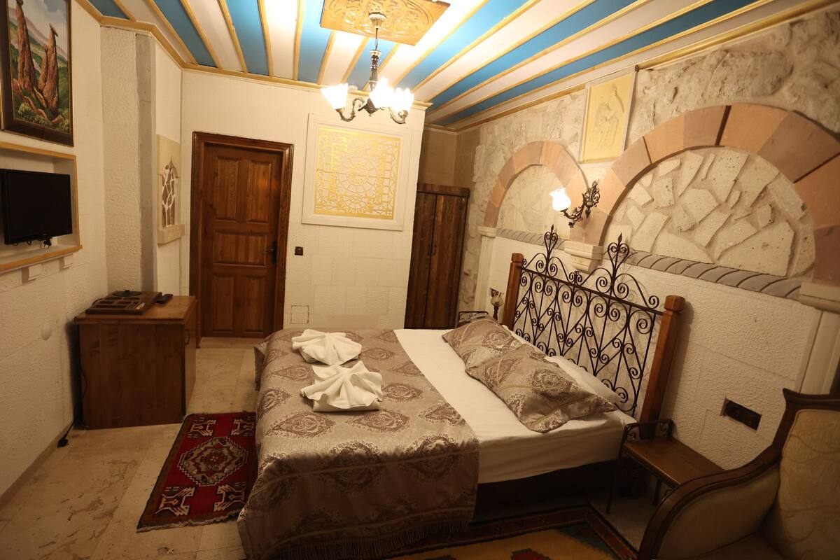 Un dormitorio con cama, mesita de noche de madera, televisor, candelabro y decoración en la pared.
