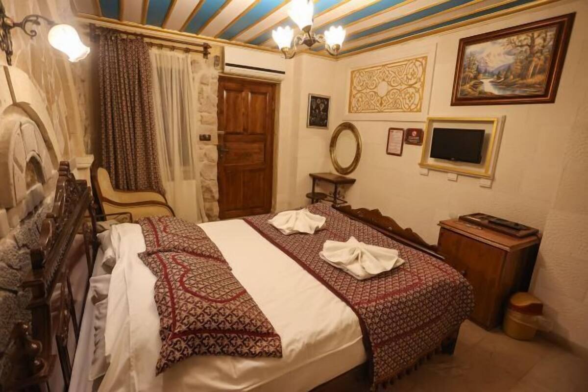 Una habitación con cama, un armario de madera, un espejo, televisor y un cuadro en la pared.