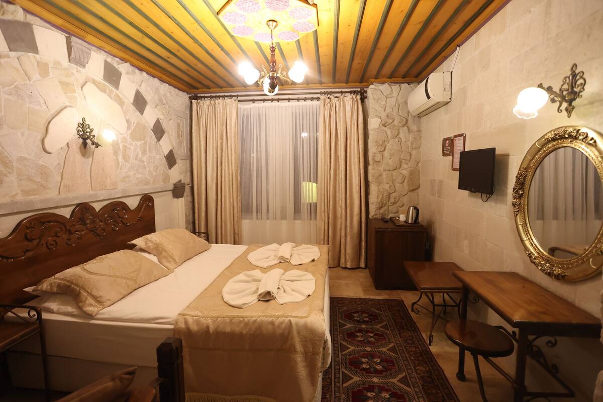Una habitación de hotel con cama, un banco de madera, un escritorio, un espejo y una araña.