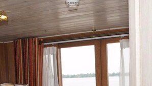 A hotel room with two beds, a view of a body of water, and a lamp on the left side. - L'Amant Cruise (Thoi Son)