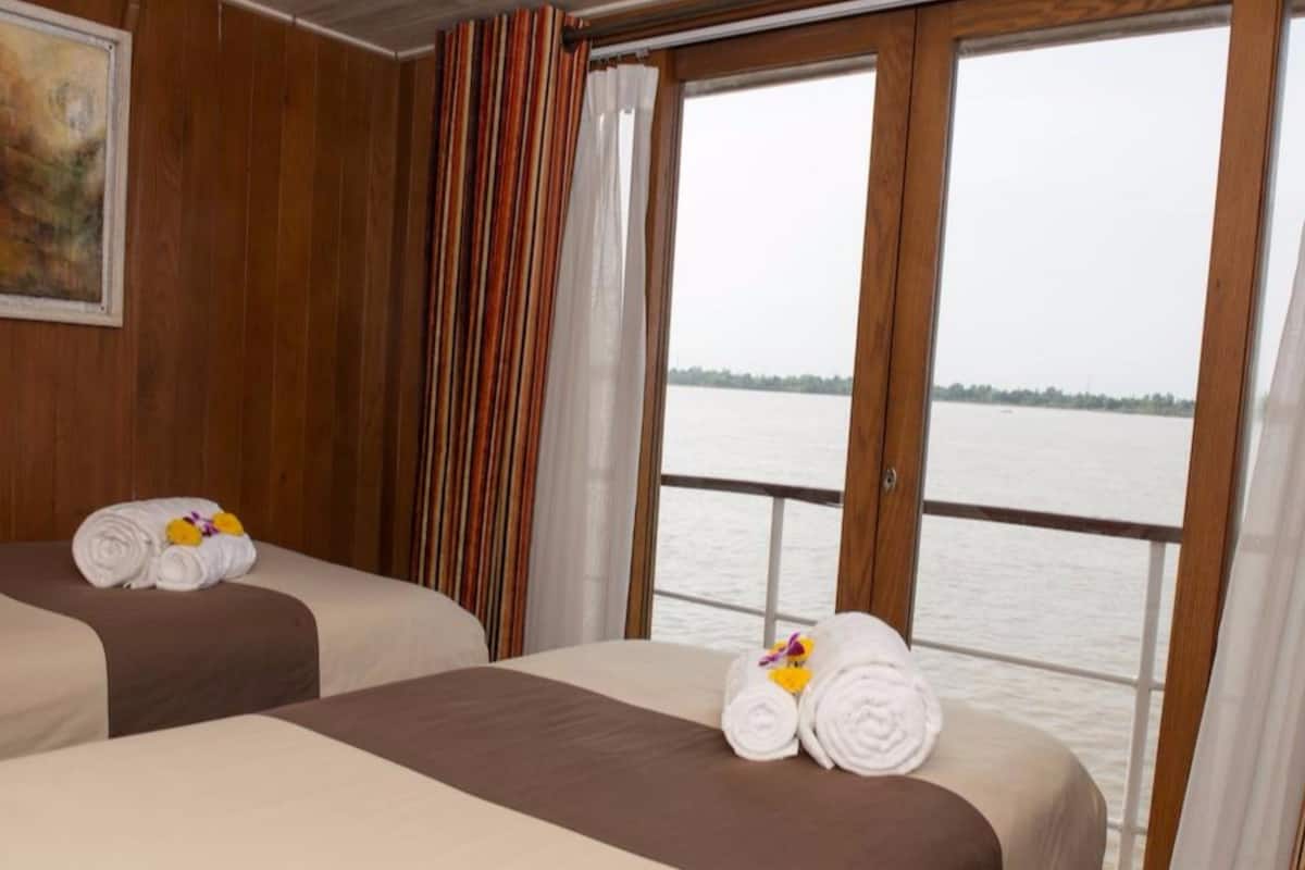 Two beds with towels, a painting, and a view of a body of water through large windows.