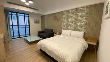 Een moderne slaapkamer met een groot bed, een kleine zithoek, een nachtkastje en uitzicht door een schuifdeur op een balkon.