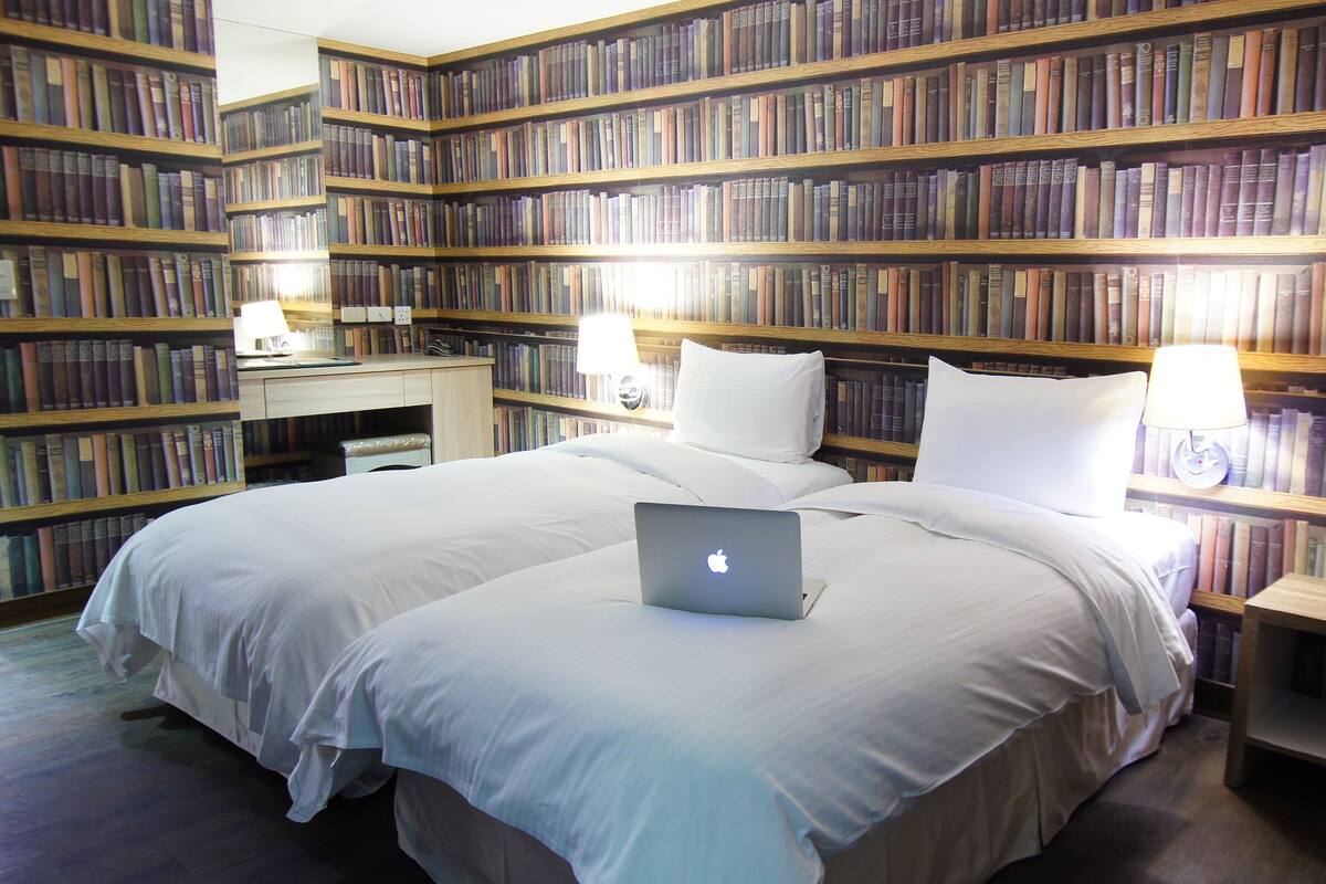 A bedroom with a large bed, two bedside tables, a desk, and a bookshelf filled with books.