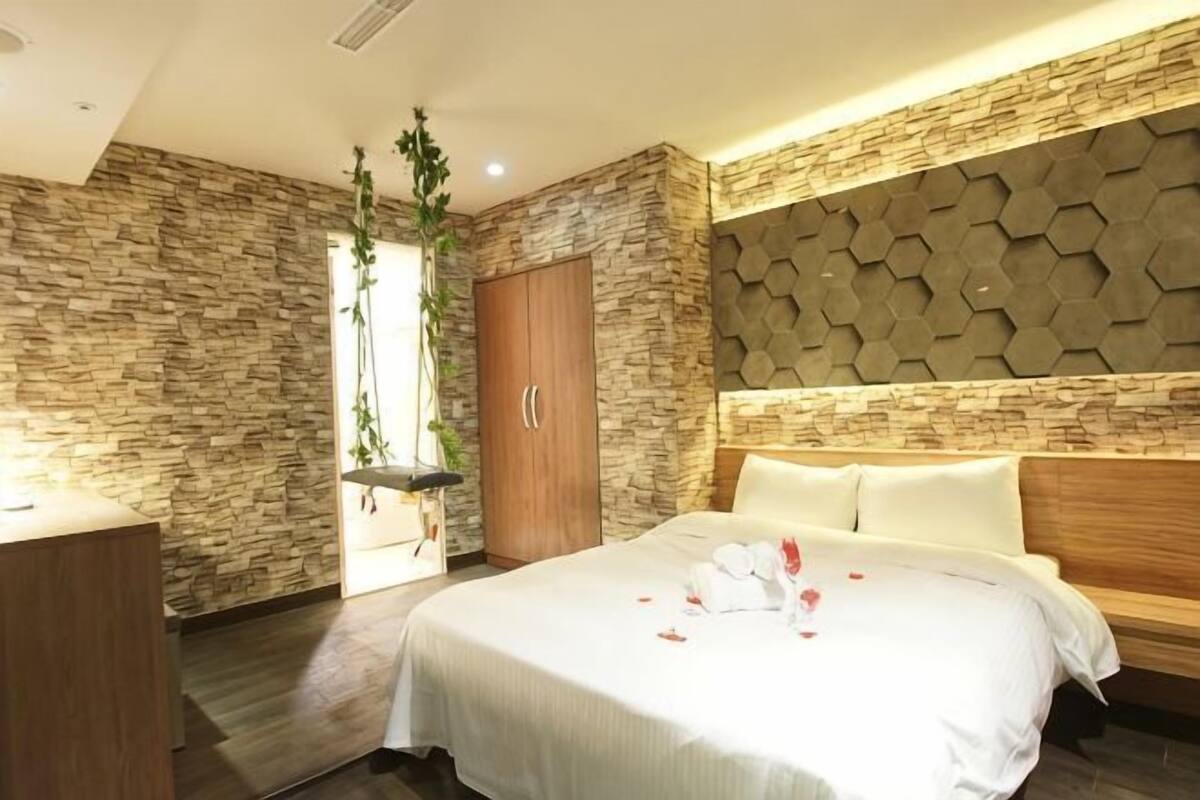 A bedroom with a stone wall, a wooden wardrobe, a bed with white bedding, and a hanging plant.