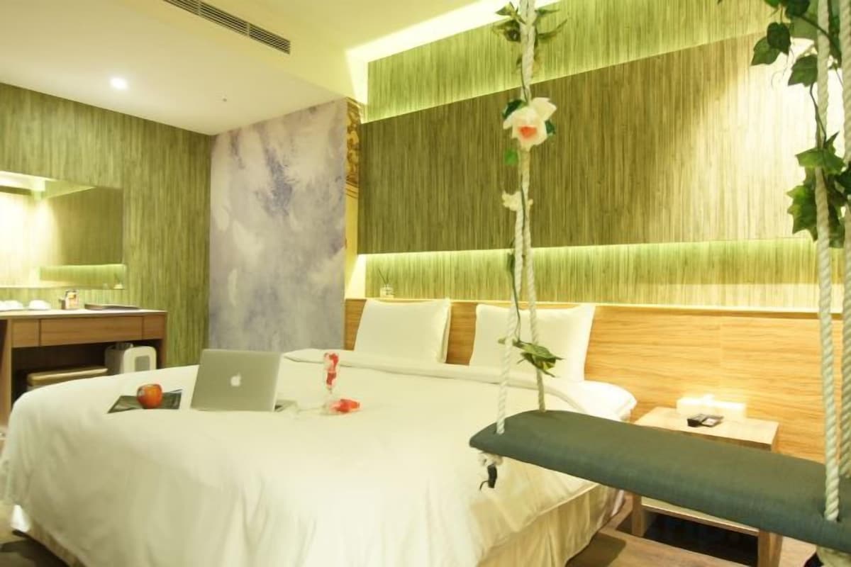 A hotel room with a bed, a desk, a laptop, and a bedside table with a lamp.