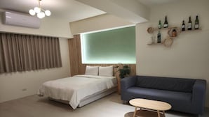 Une chambre moderne comprenant un lit, un canapé, une petite table et une étagère murale où sont posées des bouteilles.
