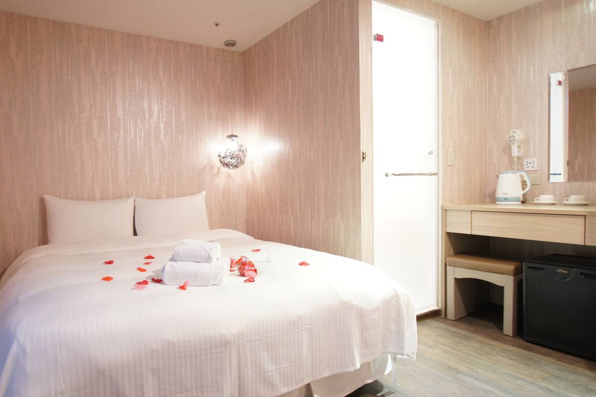 A hotel room with a bed, a bedside table, a mirror, and a small kitchenette.