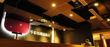 Een hotel receptie met een modern ontwerp, met een receptiebalie, een digitaal scherm en een plafond met ingebouwde verlichting.