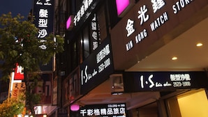 Un bâtiment dont la façade est ornée d’enseignes lumineuses indiquant la présence d’une boutique de montres et d’un salon de coiffure.