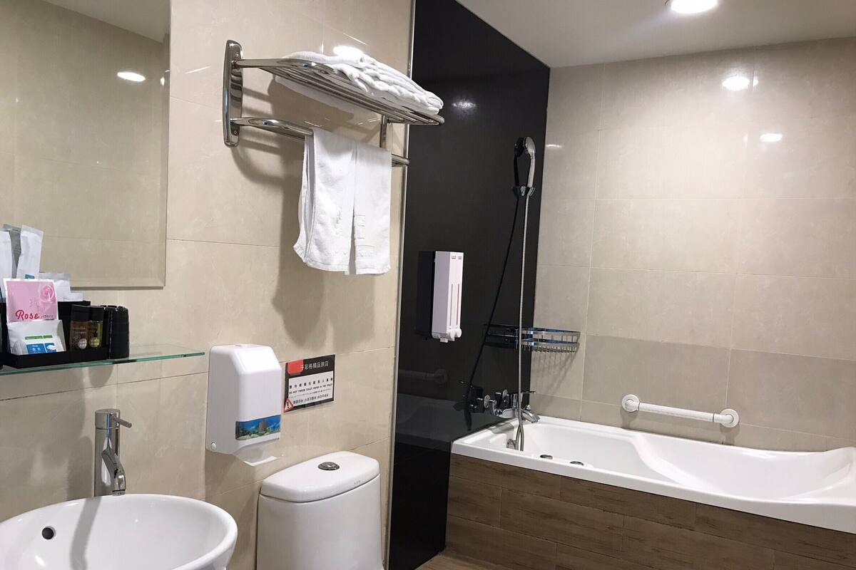 A modern bathroom with a sink, toilet, and bathtub. There is a towel rack with towels, a soap dispenser, and a sign on the wall.