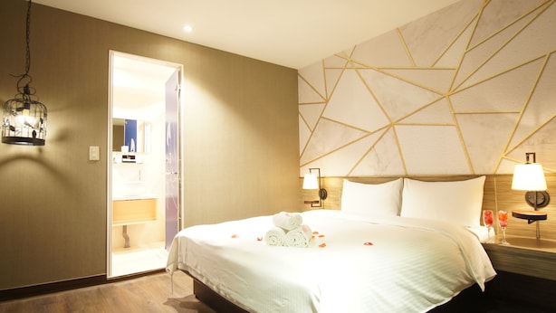 Une chambre d’hôtel avec un lit, une table de chevet avec une lampe, un mur orné de motifs géométriques et une porte donnant accès à une salle de bain.