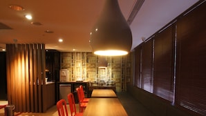 Un espace repas moderne avec une longue table en bois, des chaises rouges et un luminaire suspendu.