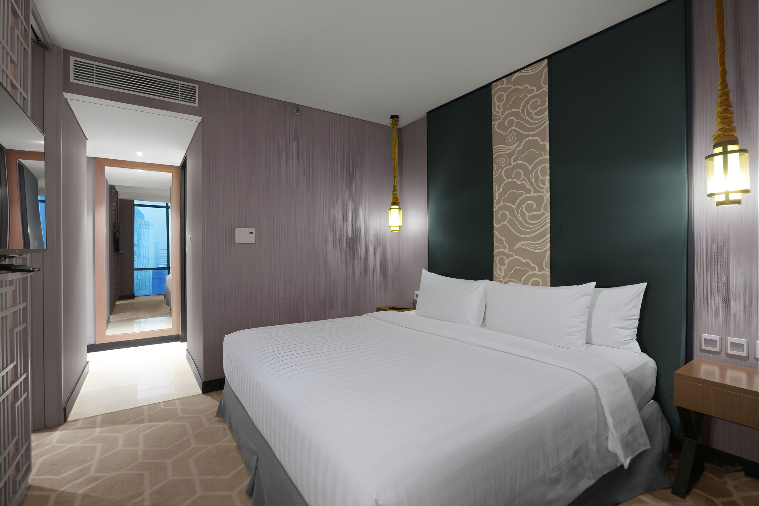 A hotel room with a large bed, a nightstand, a wardrobe, and a view of the city through the window.
