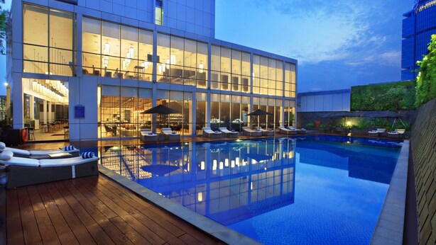 A modern hotel with a large outdoor pool, sun loungers, and a well-lit interior. - Aston Priority Simatupang Hotel & Conference Center (Jakarta)