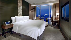 A hotel room with a large bed, a desk with a chair, a TV, and a view of the ocean. - Aston Priority Simatupang Hotel & Conference Center (Jakarta)