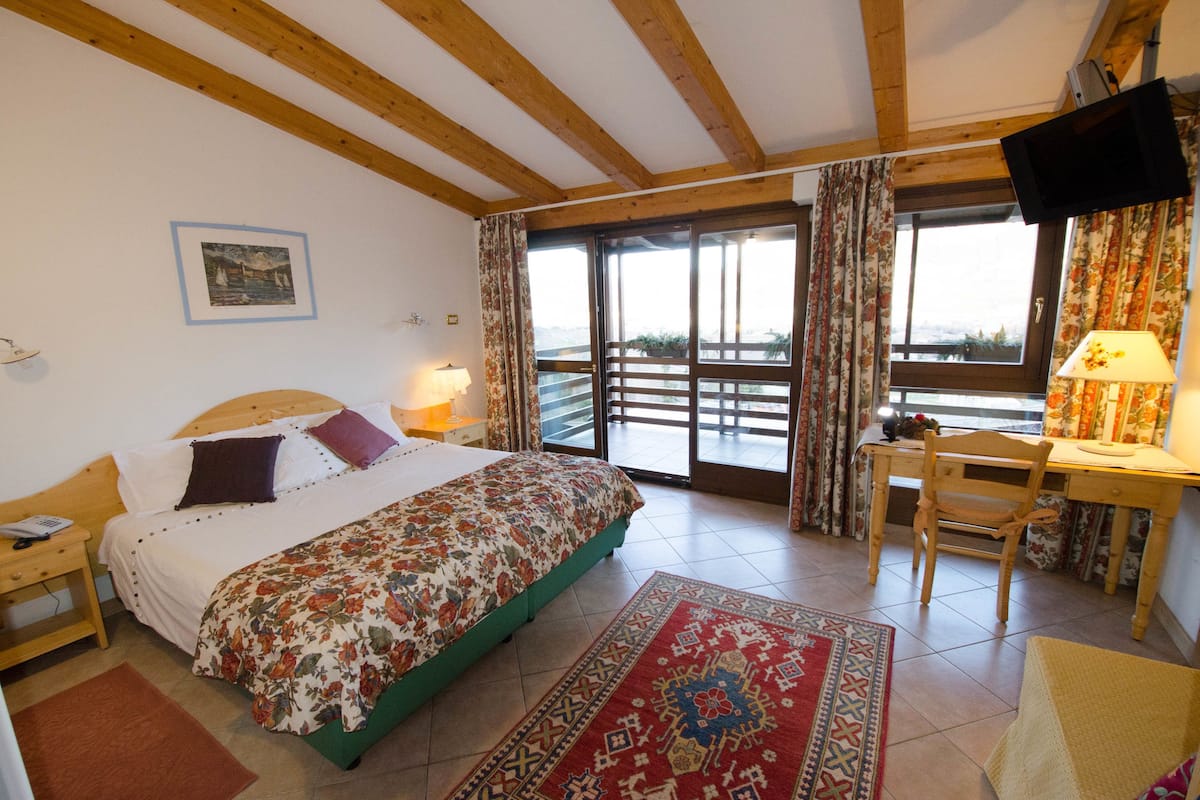 A bedroom with a bed, bedside table, lamp, and a view of the outdoors through a sliding door.