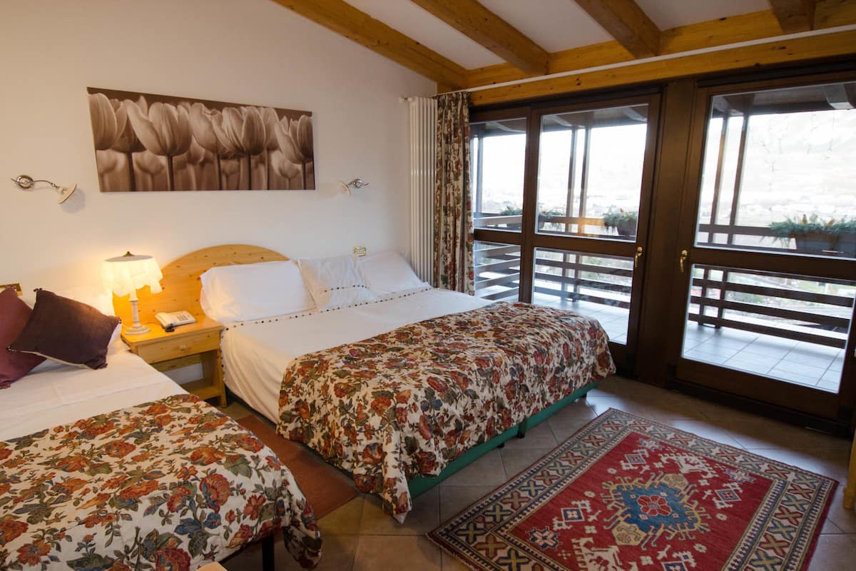 A bedroom with a large bed, a smaller bed, a nightstand, a lamp, a telephone, and a window with a view of the outside.