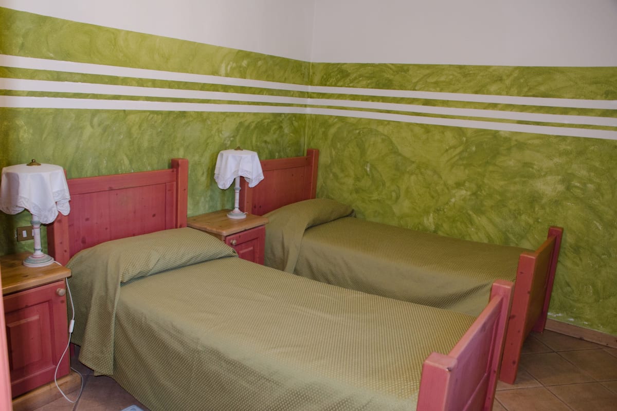 A room with two single beds, a nightstand with a lamp, and a wall with green and white stripes.