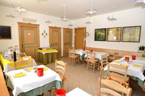 Un'area pranzo con tavoli apparecchiati, sedie di legno e un buffet con varie pietanze.