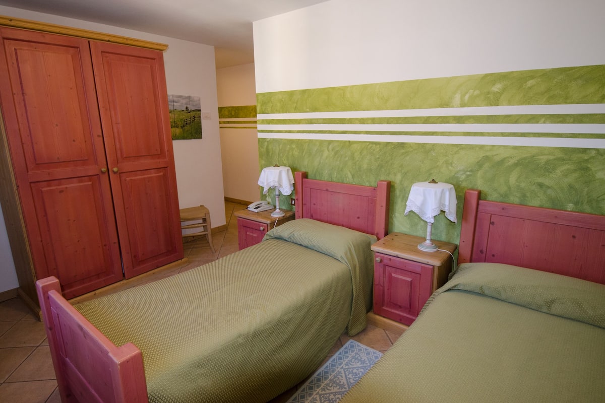 A bedroom with two beds, wooden wardrobe, and a green-striped wall.