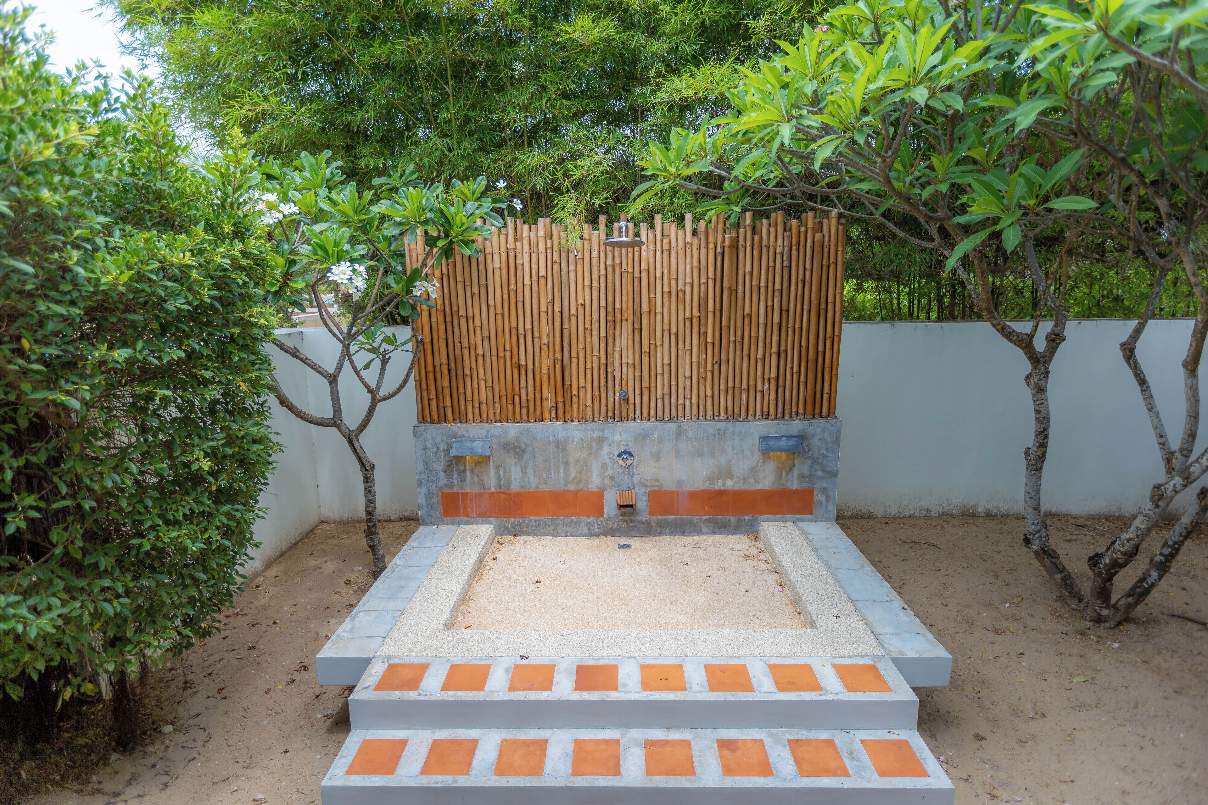 Piscina rectangular al aire libre con valla de bambú y escalones que conducen a ella, rodeada de vegetación.