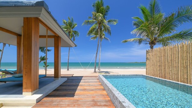 A wooden deck leading to a pool with a bamboo fence, palm trees, and a beach view. - Sirarun Resort (Thap Sakae)